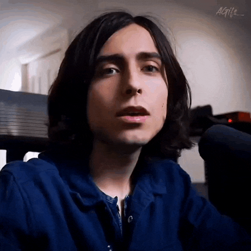 a young man with long hair is wearing a blue shirt