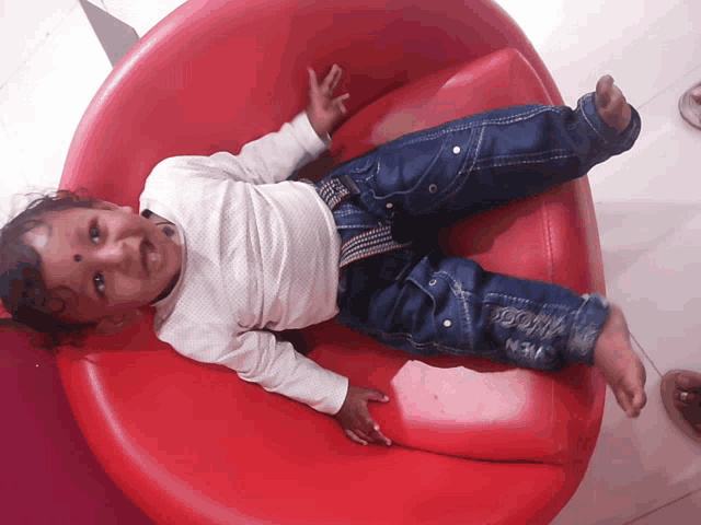 a baby is laying on a red chair with a white shirt on