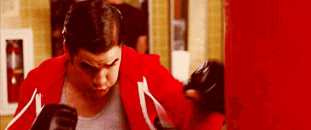 a man in a red jacket and black boxing gloves is punching a punching bag .