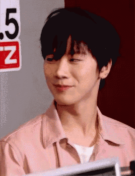 a young man in a pink shirt is smiling in front of a sign that says 5 n