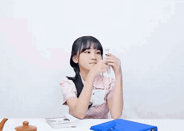a young girl is sitting at a table with a blue folder and a book