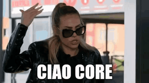a woman wearing sunglasses and a leather jacket is standing in front of a sign that says ciao core .