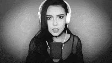 a woman wearing headphones and a choker is singing into a microphone .