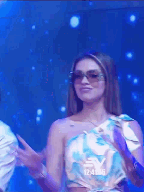 a woman wearing sunglasses and a floral top is dancing on a stage .