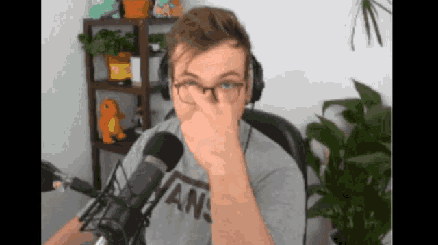 a man wearing glasses and a vans shirt is covering his nose in front of a microphone