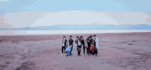 a group of people standing on a beach with mountains in the background and the word cuksou on the bottom right