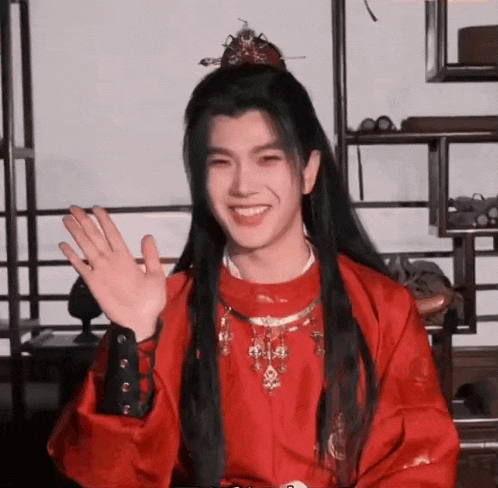 a man with long black hair is wearing a red robe and a crown .