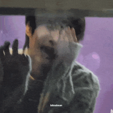 a close up of a person covering their face with their hands behind a glass door .