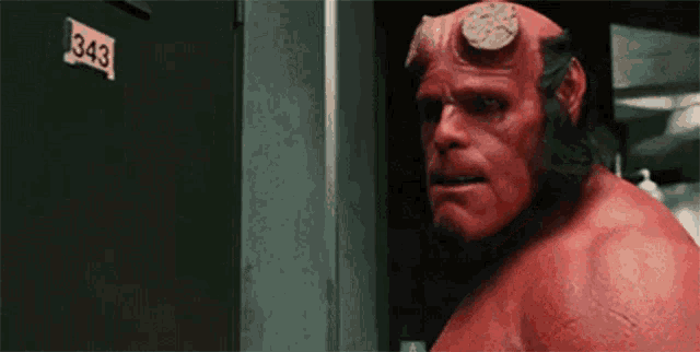 a red monster with horns is standing in front of a door with the number 343 on it .