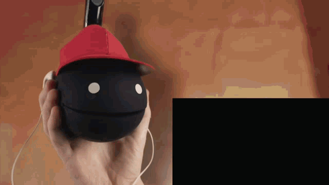 a person wearing a red hat is holding a black ball with a face on it