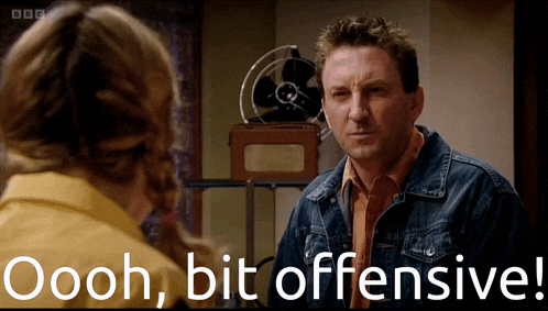a man in a denim jacket is talking to a woman with the words oooh bit offensive behind him