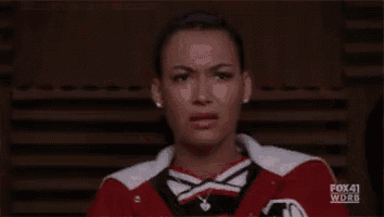 a woman in a cheerleading uniform is making a funny face while sitting in a chair .