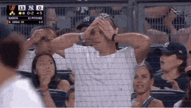 a new york yankees fan holds her head while watching a game