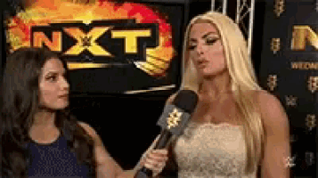 two women are standing in front of a sign that says nxt .