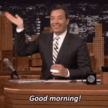 a man in a suit and tie is saying good morning while sitting at a table .