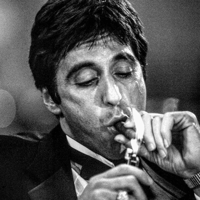 a man in a suit and tie is lighting a cigarette with a lighter