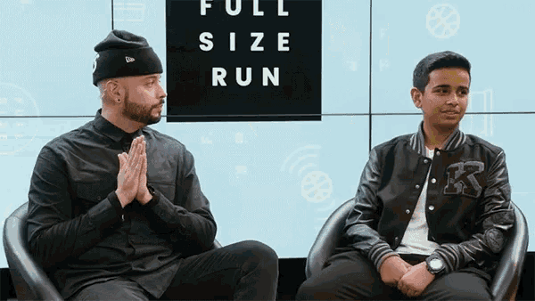two men sit in chairs in front of a wall that says full size run