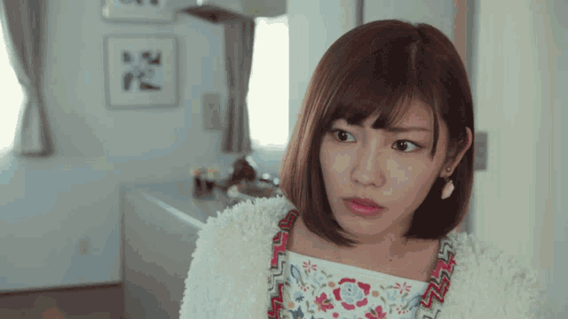 a woman wearing a white sweater and a floral top looks to the side
