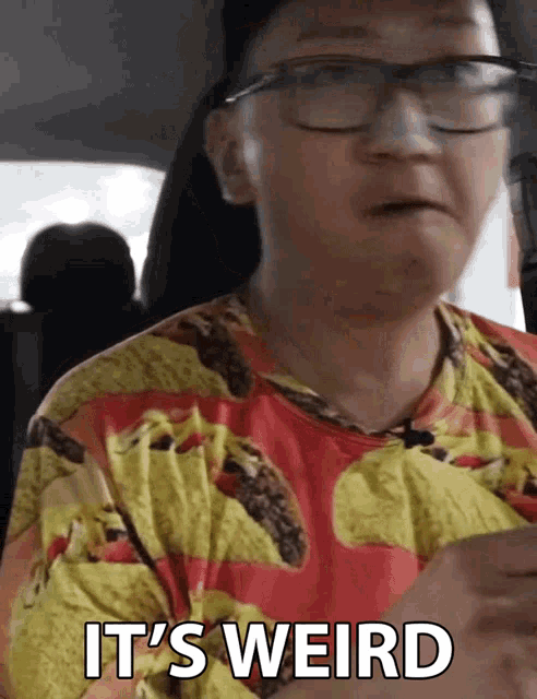 a person wearing glasses and a shirt with tacos on it says it 's weird