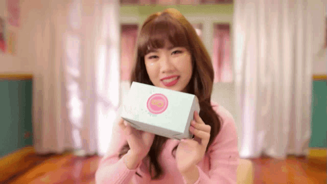 a woman in a pink sweater is holding a white box with a pink circle on it .