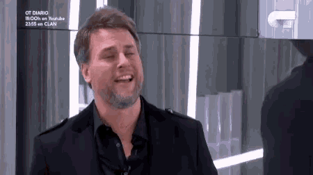 a man with a beard is smiling in front of a mirror while wearing a black suit .