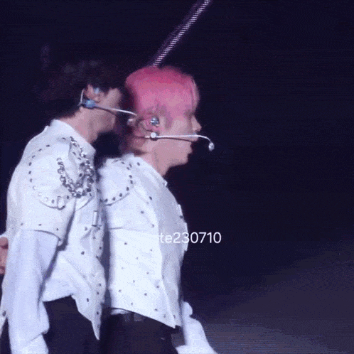 two men are standing next to each other on a stage and one has pink hair