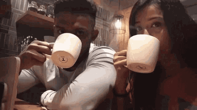 a man and a woman are sitting at a table drinking coffee from cups .