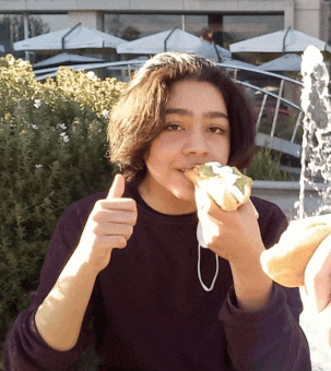 a young girl eating a sandwich and giving a thumbs up