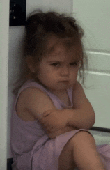 a little girl with her arms crossed is sitting on the floor