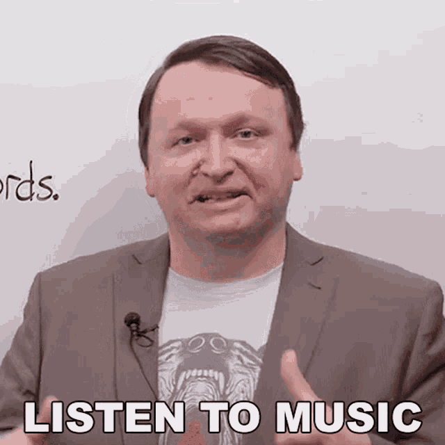 a man in a suit says listen to music in front of a white wall