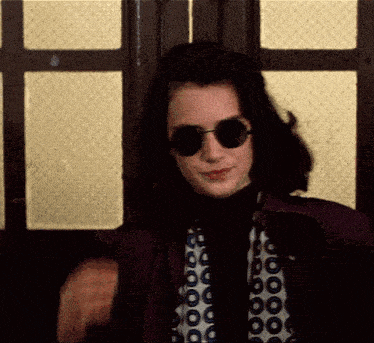 a woman wearing sunglasses is standing in front of a window