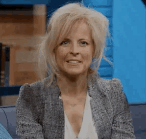 a woman is sitting on a couch wearing a blazer and a white shirt .