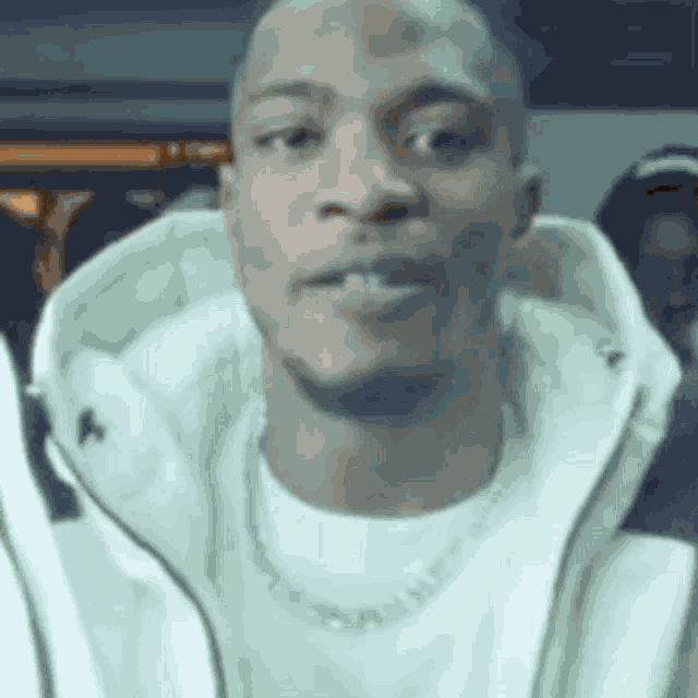 a man wearing a white jacket and a white t-shirt is looking at the camera .