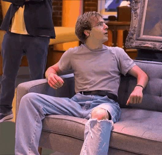 a young man sits on a couch with a painting behind him