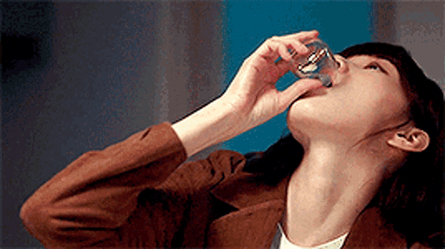 a woman in a brown jacket is drinking from a glass with her mouth open .
