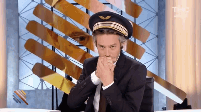 a man in a pilot 's hat is sitting at a desk with his hands folded