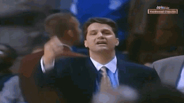 a man in a suit and tie stands in front of a screen that says hardwood classics on it
