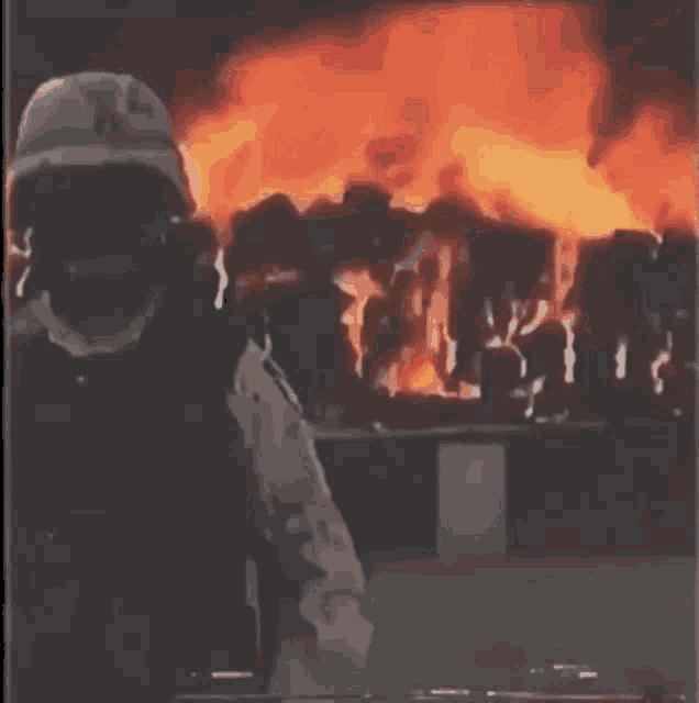 a man in a helmet stands in front of a fire .