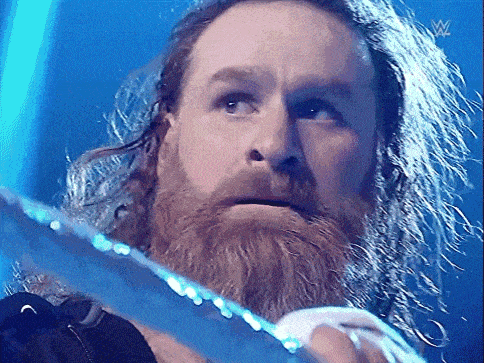 a man with a beard and long hair is holding a sword in front of a blue background .