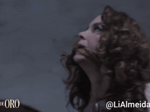 a woman with curly hair is looking up with the words de oro in the corner