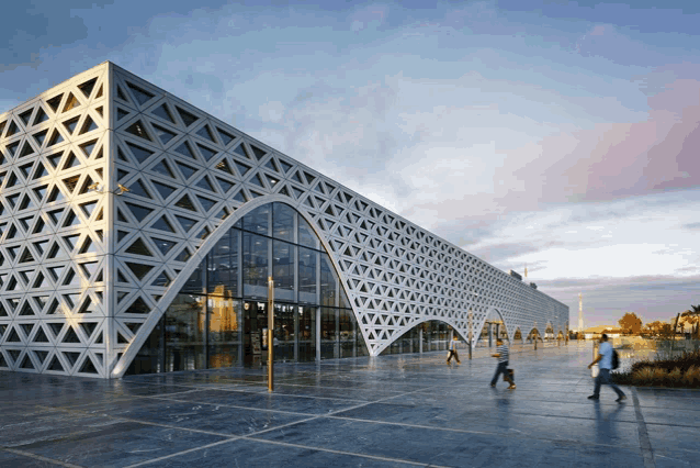 people walking in front of a large building with a geometric pattern
