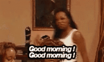 a woman in a white tank top is standing in a living room and says `` good morning '' .
