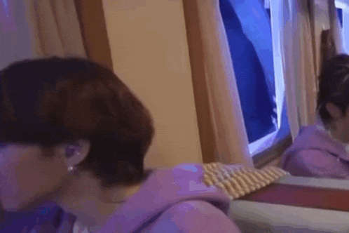 a man in a purple hoodie is sitting in front of a mirror in a room .