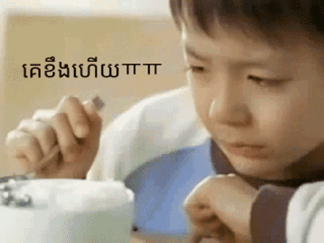 a young boy is sitting at a table with a fork in his hand and a foreign language behind him .