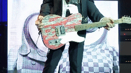 a man in a suit is playing a guitar in front of a large screen