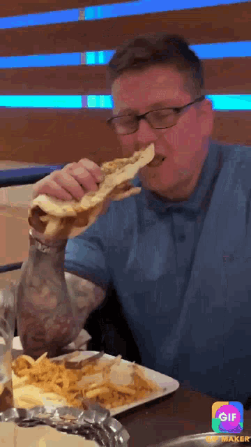 a man with glasses is eating a sandwich and french fries at a restaurant .