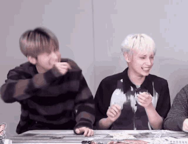 two young men are sitting at a table laughing and smiling