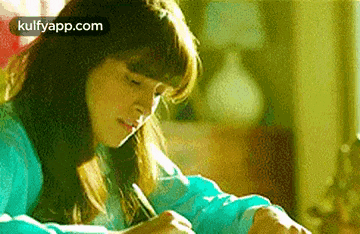 a woman is sitting at a table writing on a piece of paper with a pen .