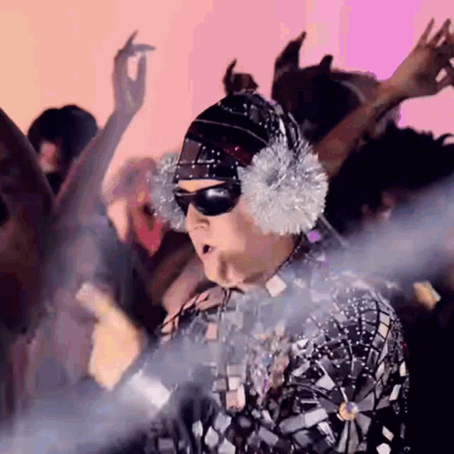 a man wearing sunglasses and ear muffs is dancing in a crowd of people .