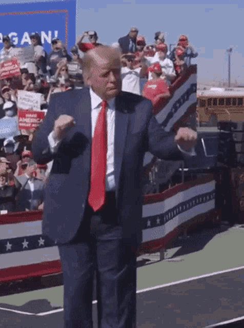 a man in a suit and tie is dancing in front of a crowd with a sign that says again